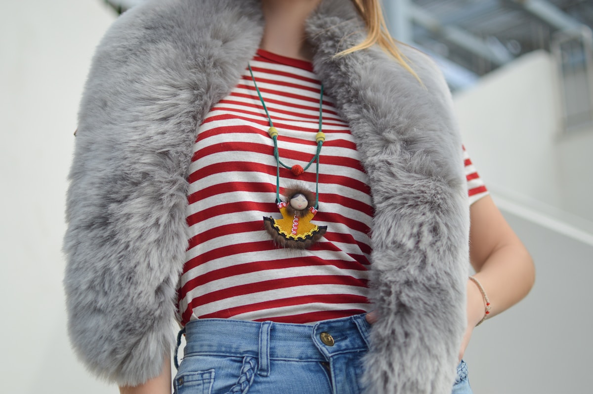 A striped top, grey vest, pendant necklace, and jeans shown together in an outfit detail